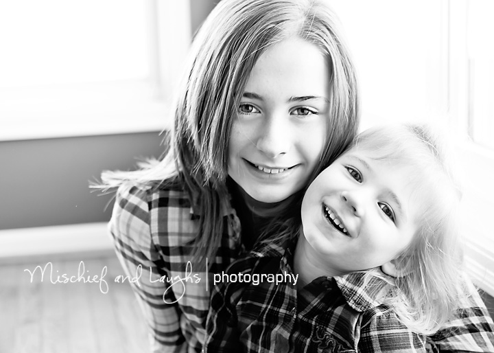 Sisters cuddle and laugh in front of the beautiful window light.