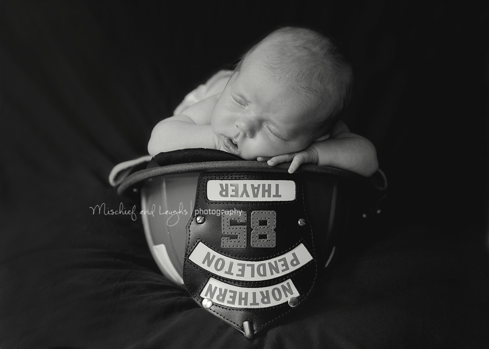 Newborn baby in a fireman's hat, black and white photograph
