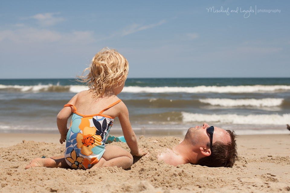 little girl burying her daddy in the sand