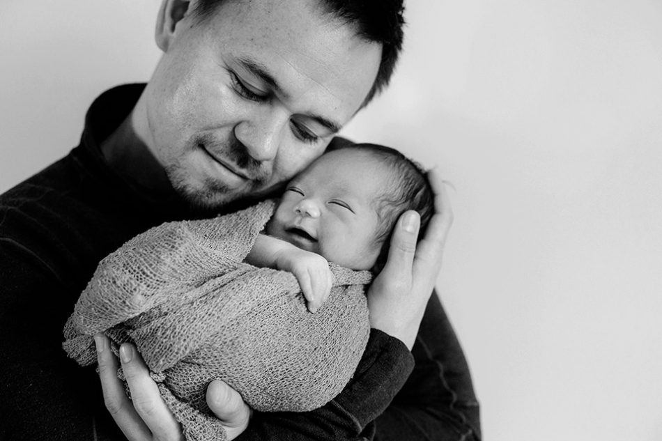 Newborn baby smiles while held by his father 