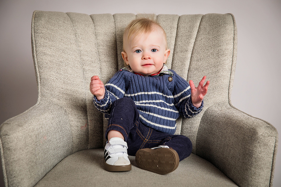 One-year-old baby boy sitting on a gray background for a classic milestone session.