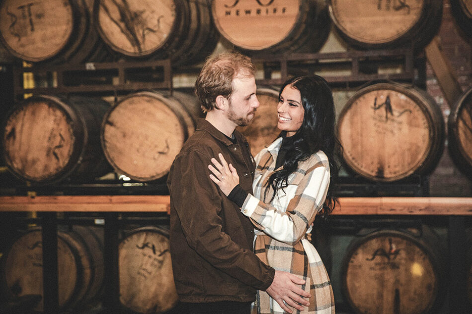 Groom-to-be lifting fiancée in front of brewery tanks